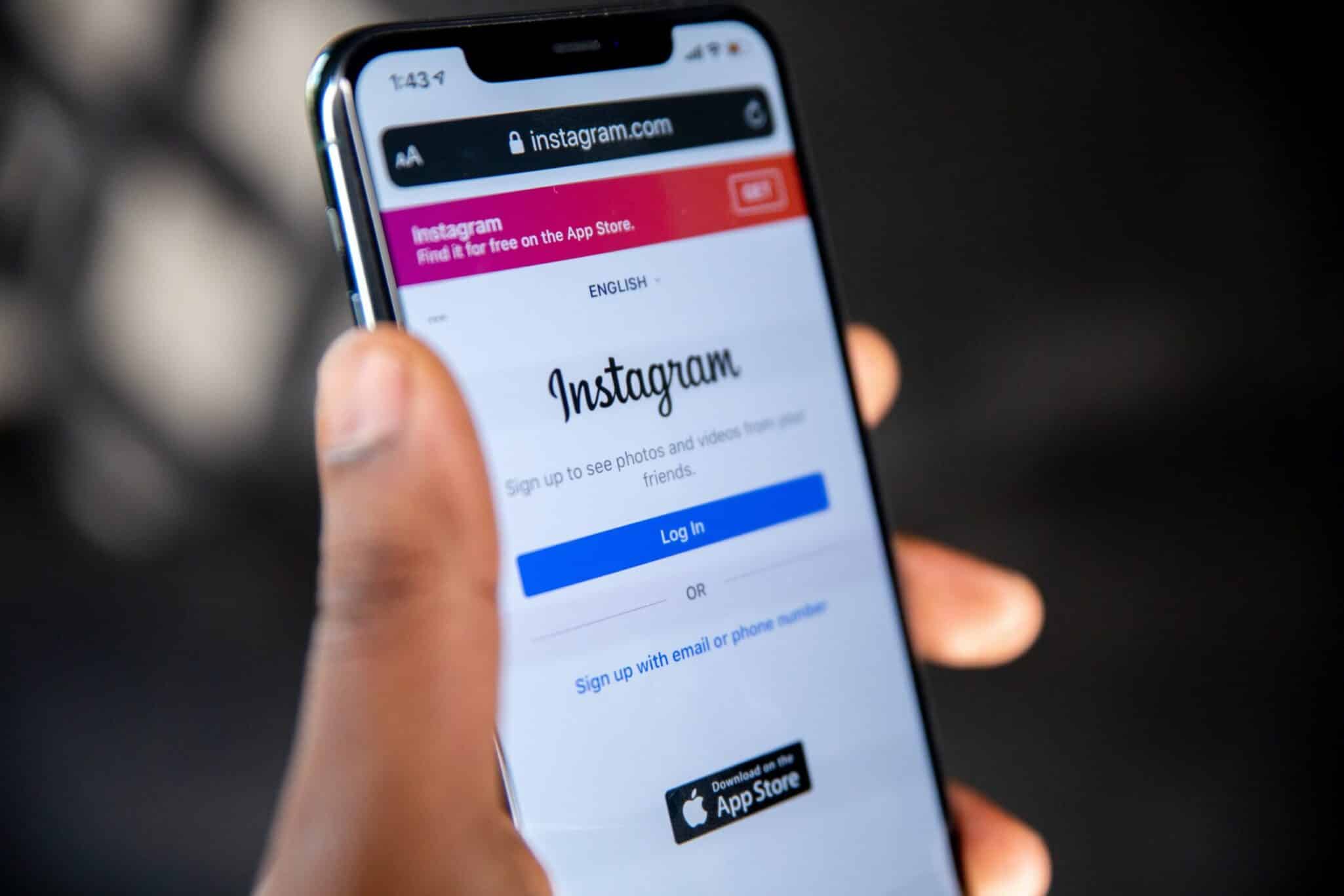 A hand holding a phone showing the Instagram login screen.