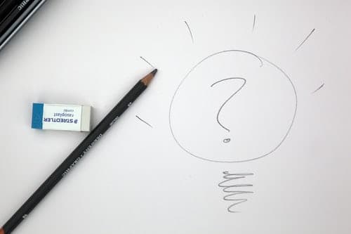 A pencil sketch of a lightbulb with a question mark inside it, drawn on white paper beside a pencil and eraser.