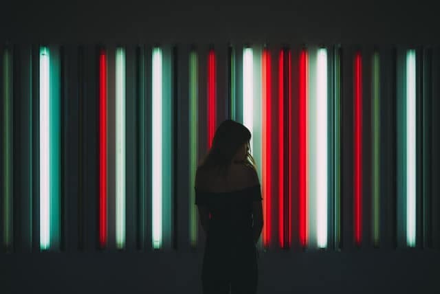 A person silhouetted against a wall of vertical red and white neon strip lights.