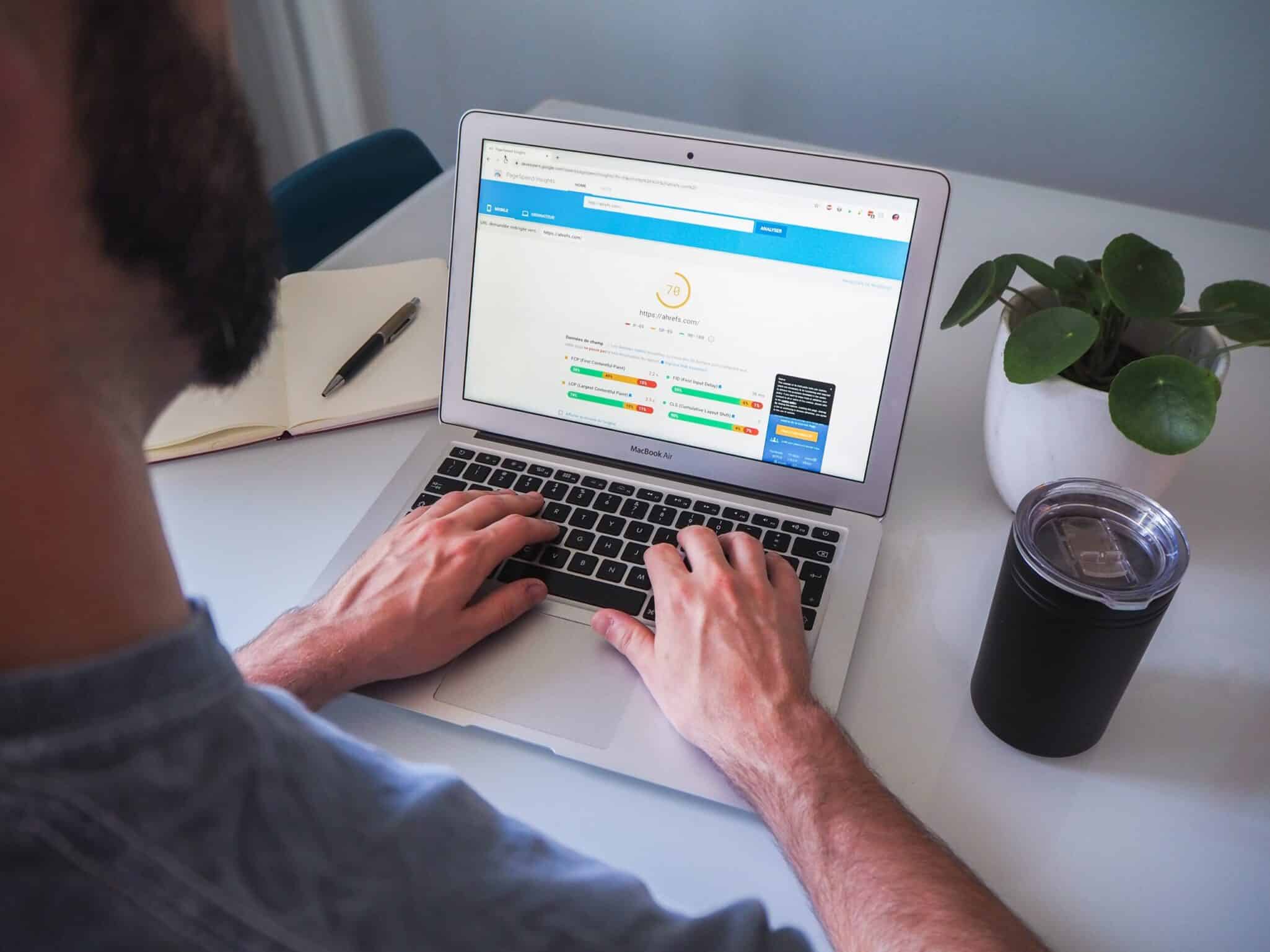 A man filling in an online form on a laptop at a white desk.