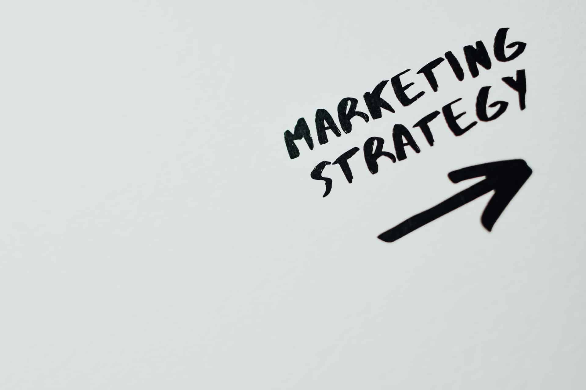 The words Marketing Strategy handwritten in black marker beside an arrow, on a white background.