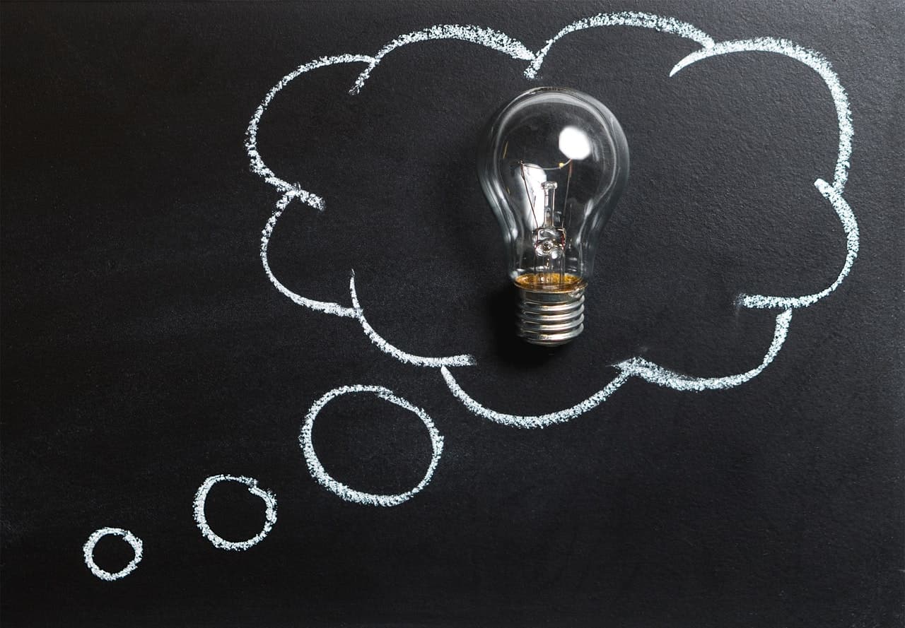 A real lightbulb placed inside a thought bubble drawn in chalk on a blackboard.