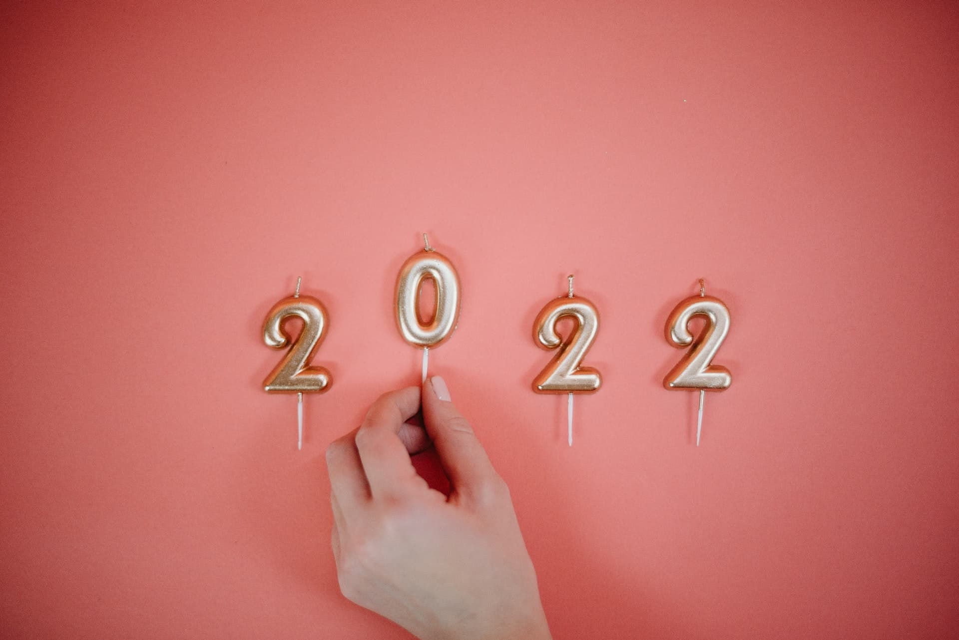 A hand arranging numbered candles spelling 2022 against a pink background.