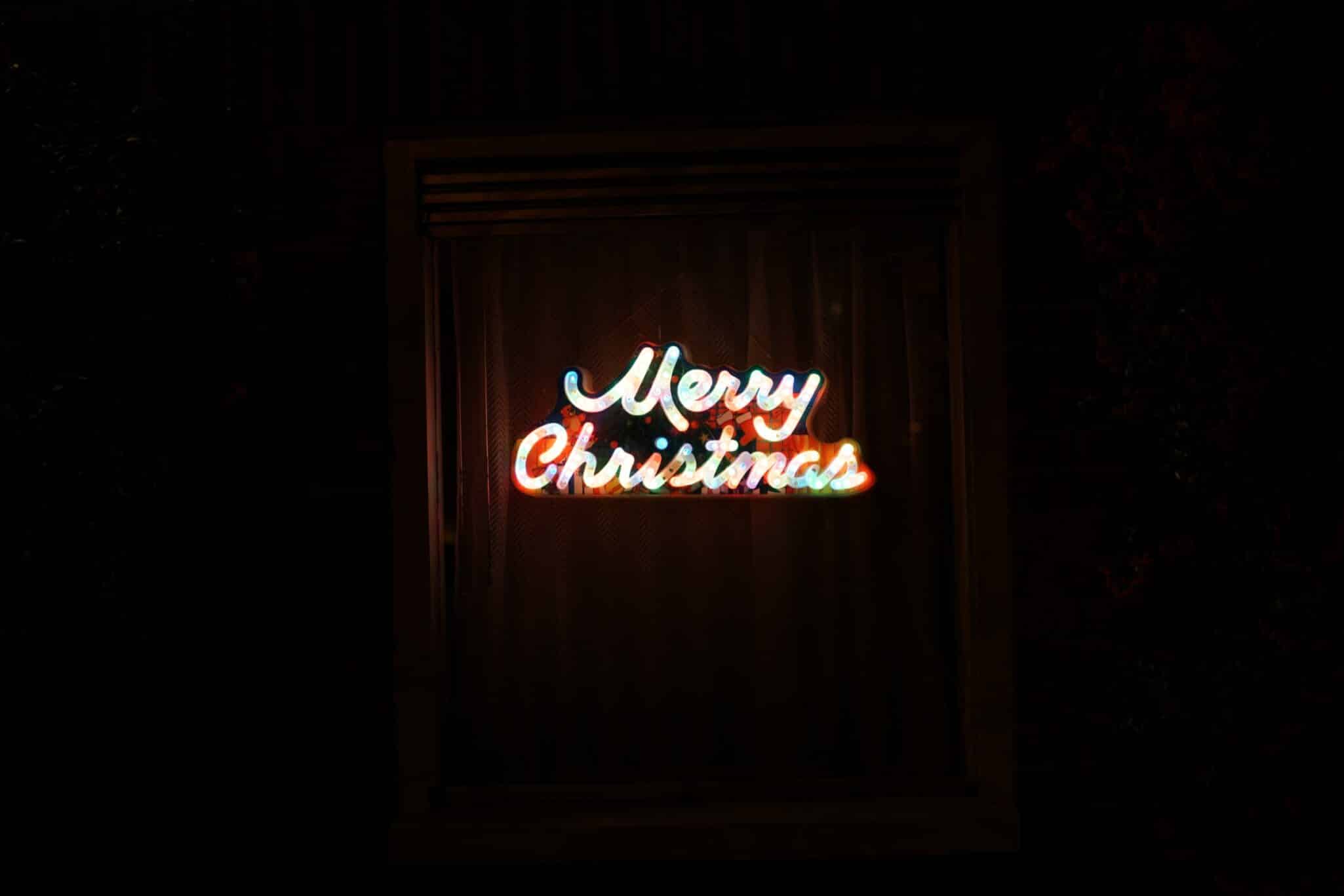 A Merry Christmas neon sign glowing in a dark window.