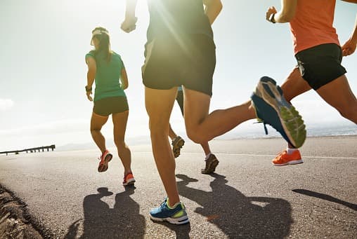 A group of runners on a sunlit road, photographed from ground level.