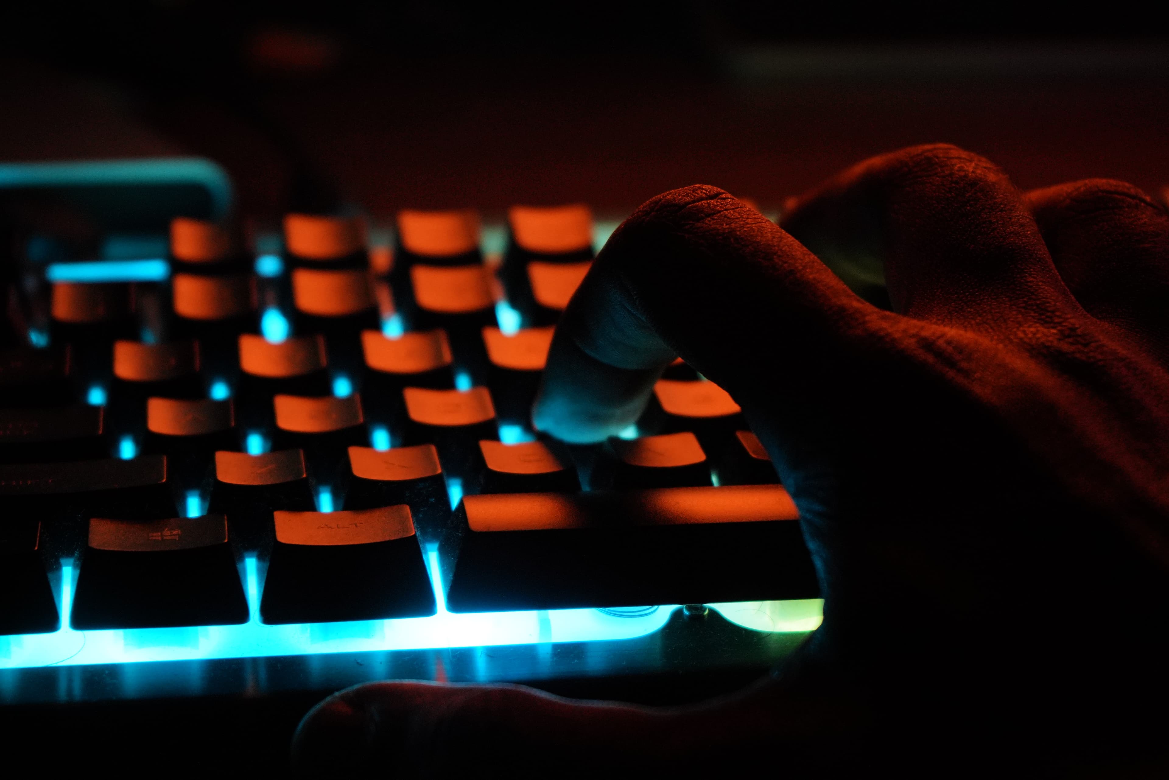 A hand typing on a backlit mechanical keyboard in a darkened room.