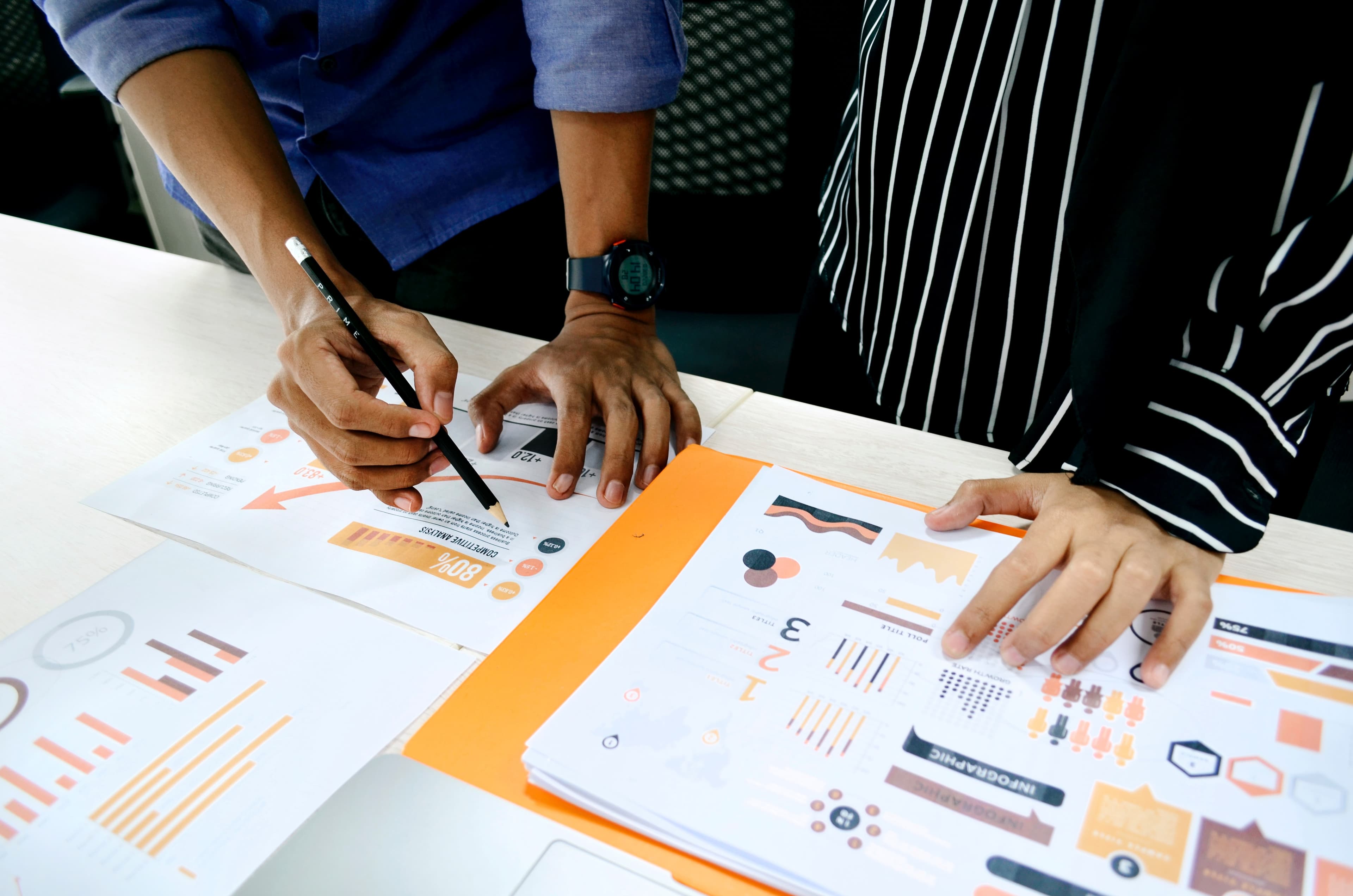 Two colleagues reviewing printed charts and graphs spread across a desk.