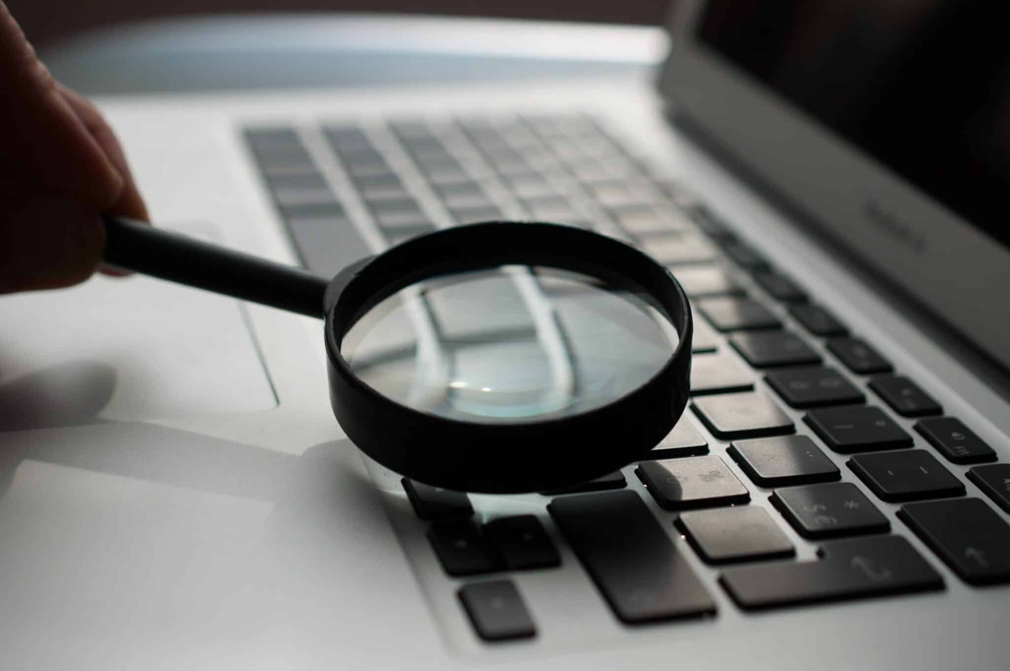 A magnifying glass held over a laptop keyboard.