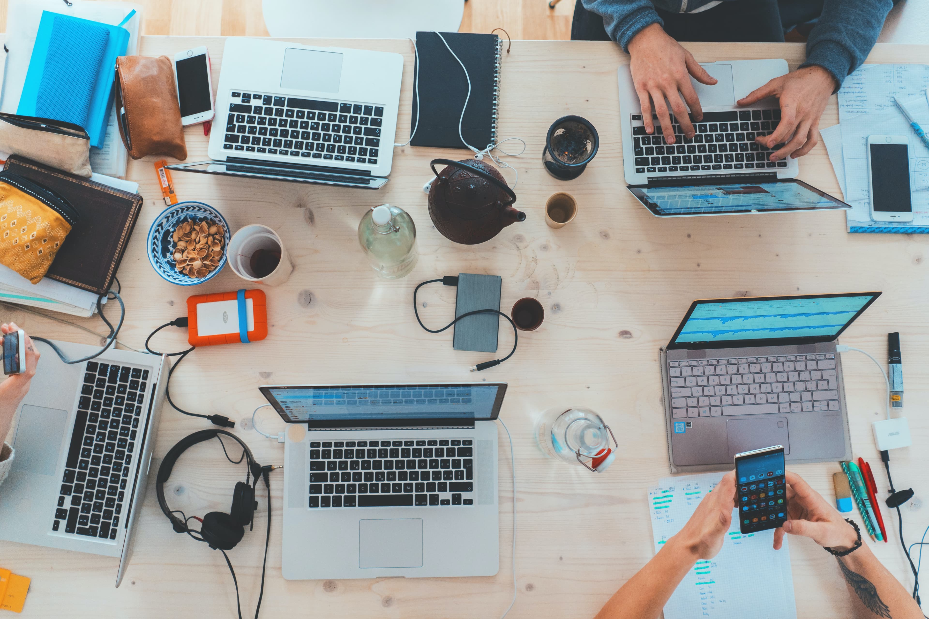 Overhead view of a team working around a table covered in laptops, phones and coffee cups.