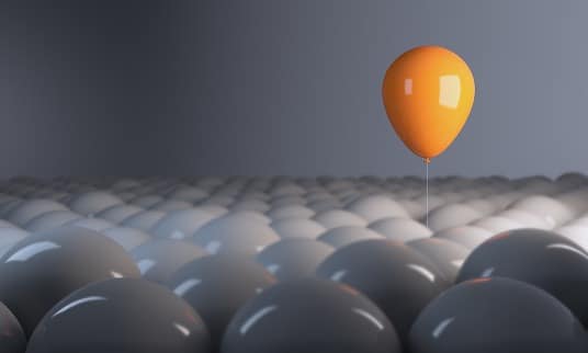 A single orange balloon rising above a crowd of identical grey balloons.