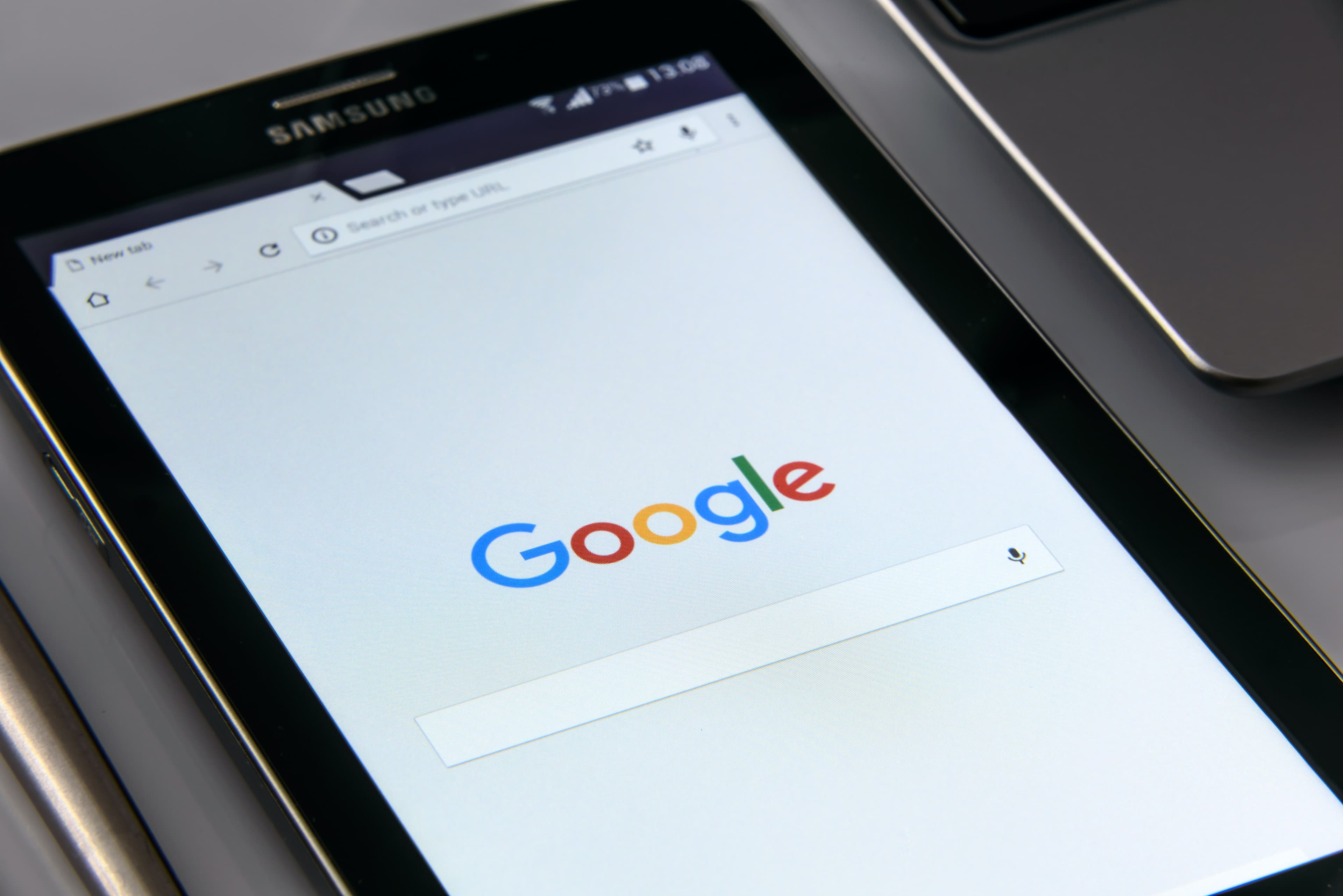 A phone resting on a laptop, showing the Google search homepage.