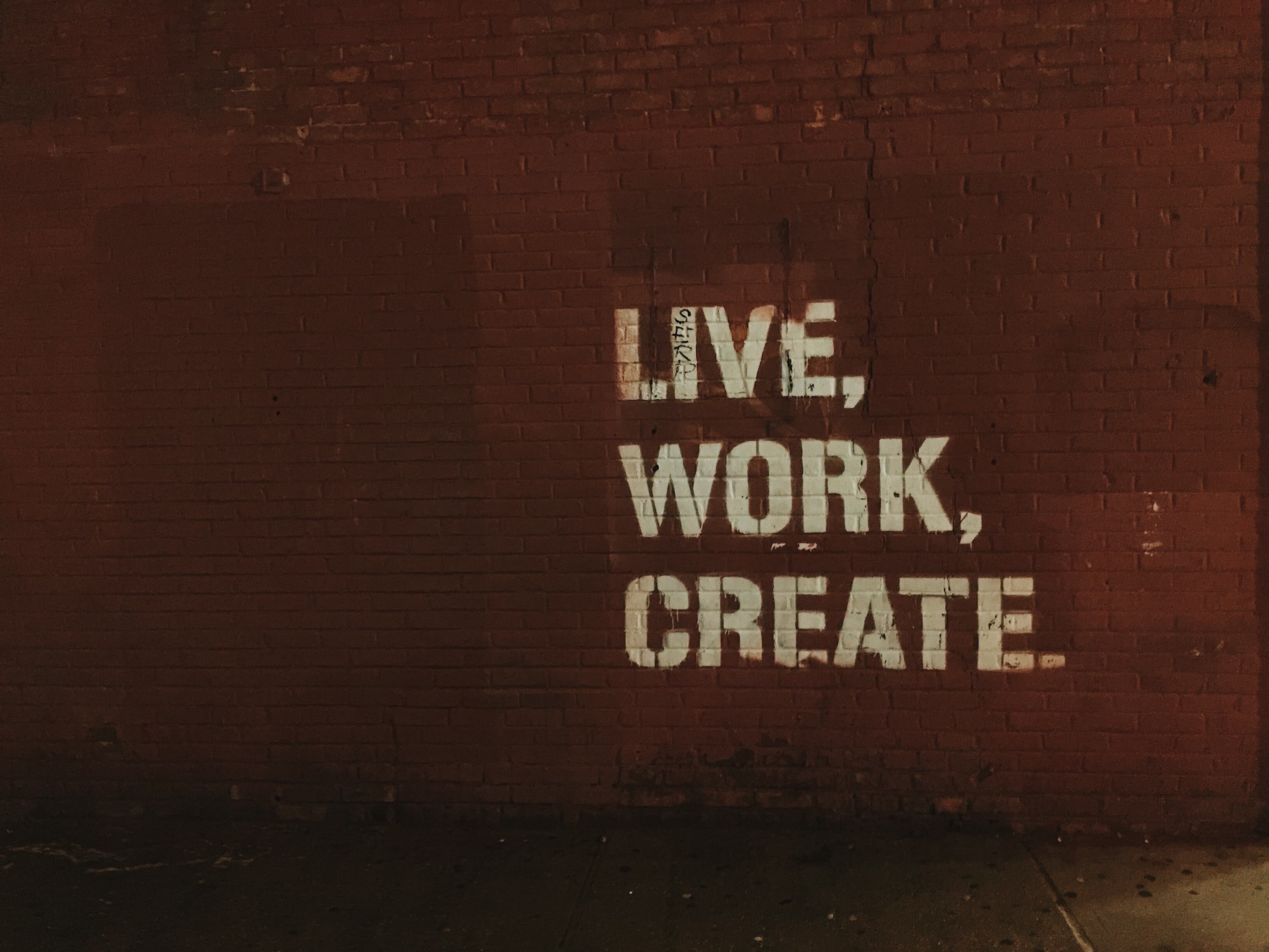 The words Live, Work, Create stencilled in white on a dark brick wall.