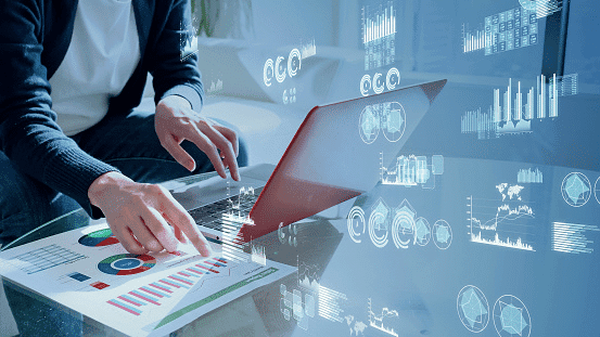 A person working at a laptop with data charts and graphs overlaid across the image.