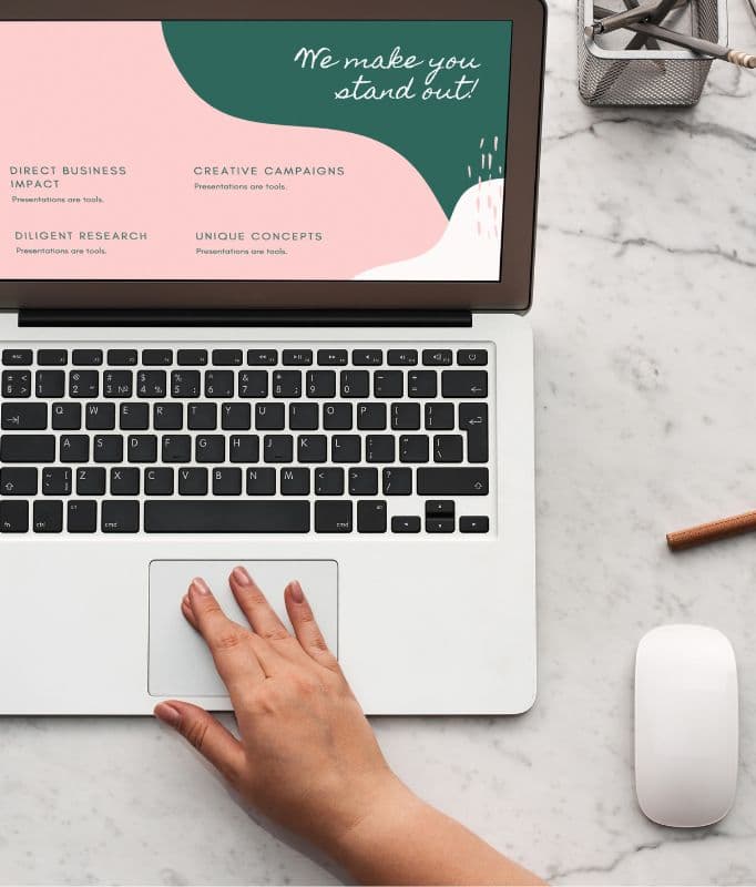 A hand on a laptop trackpad, the screen showing a pastel brand presentation reading We make you stand out.