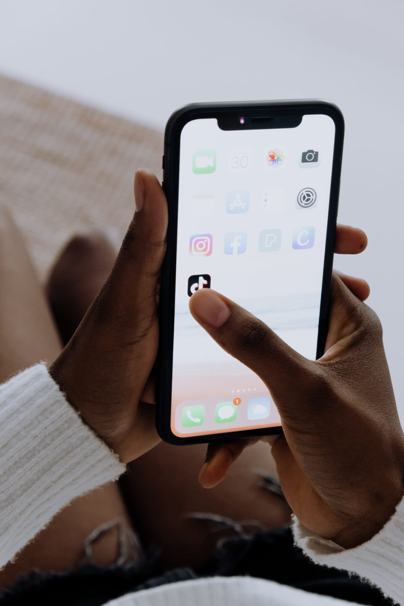 A person holding a phone showing a home screen of social media apps.