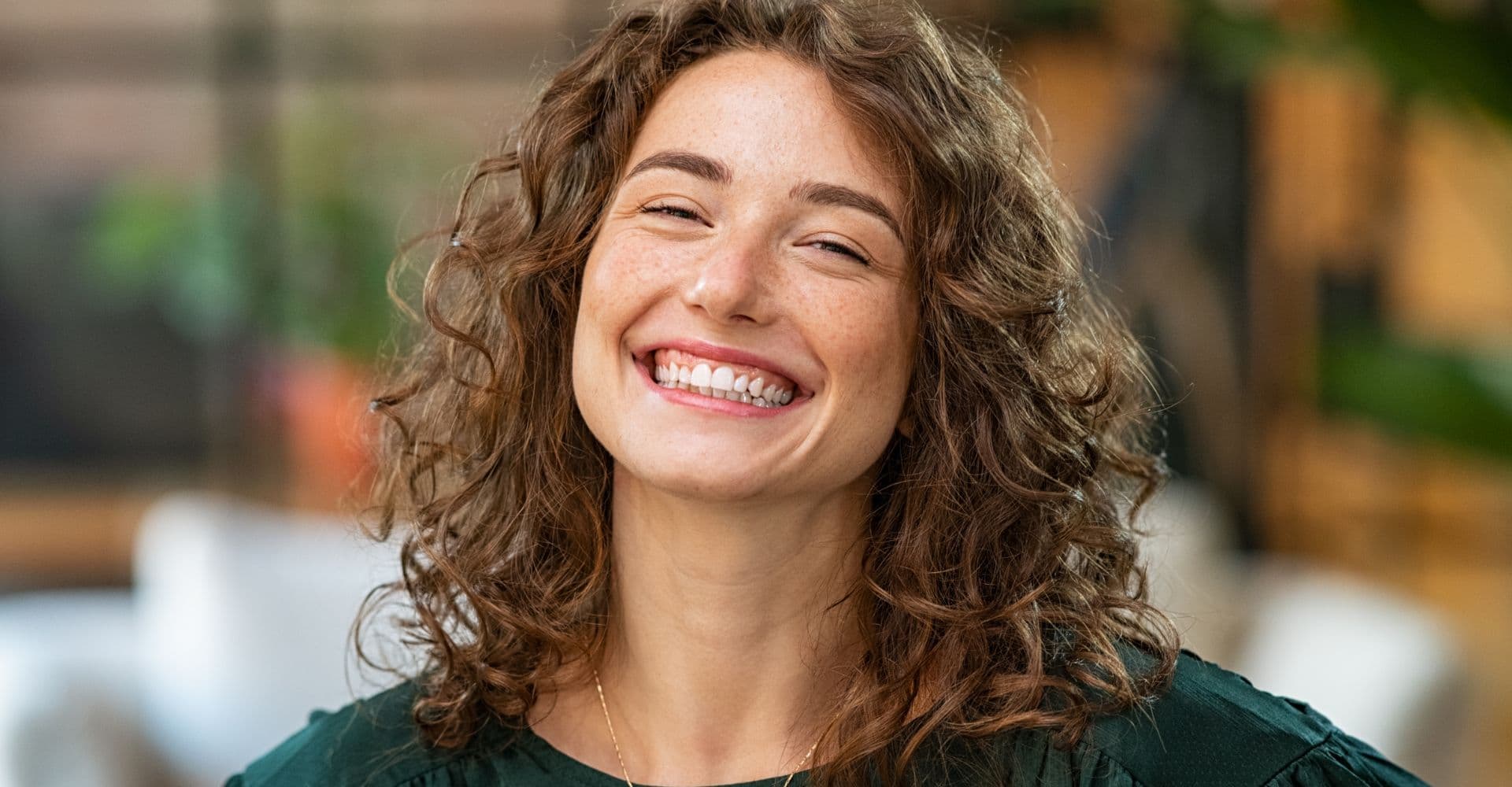 A woman with curly hair smiling broadly to camera.
