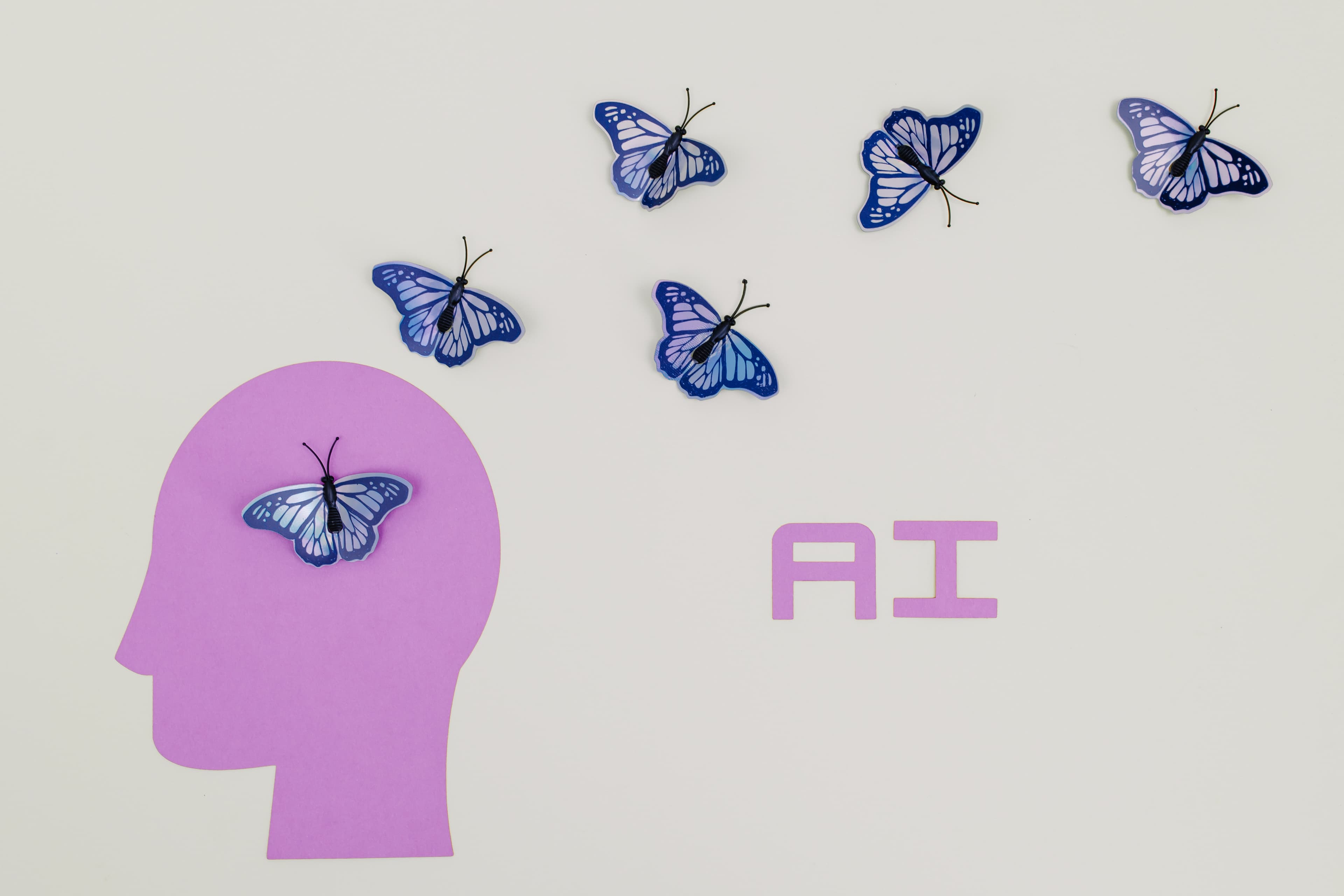 Profile of a head bust in pink with blue butterflies flying away from the head and the letters AI written to the right of the head in pink