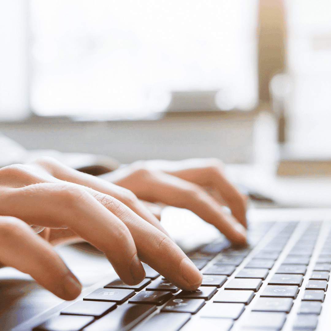 Close-up of hands typing on a laptop keyboard in a bright room.