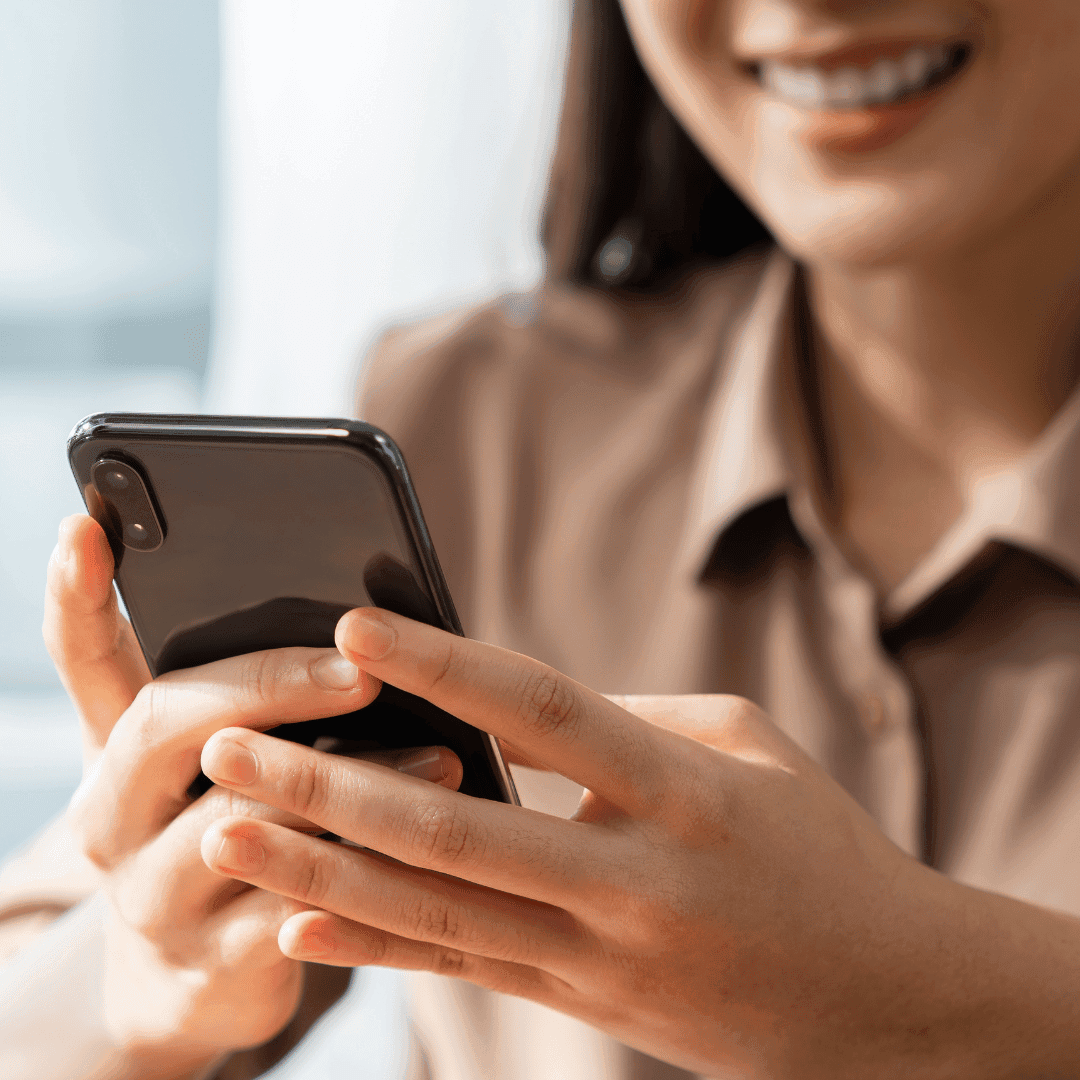 A smiling woman using a smartphone with both hands.