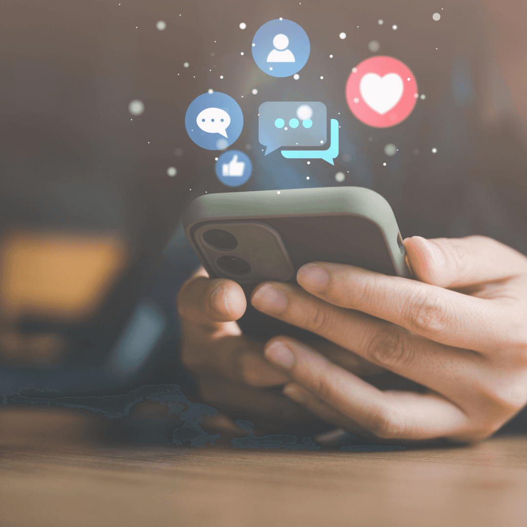 Hands holding a phone with social media reaction icons, likes, hearts and comments, floating above the screen.