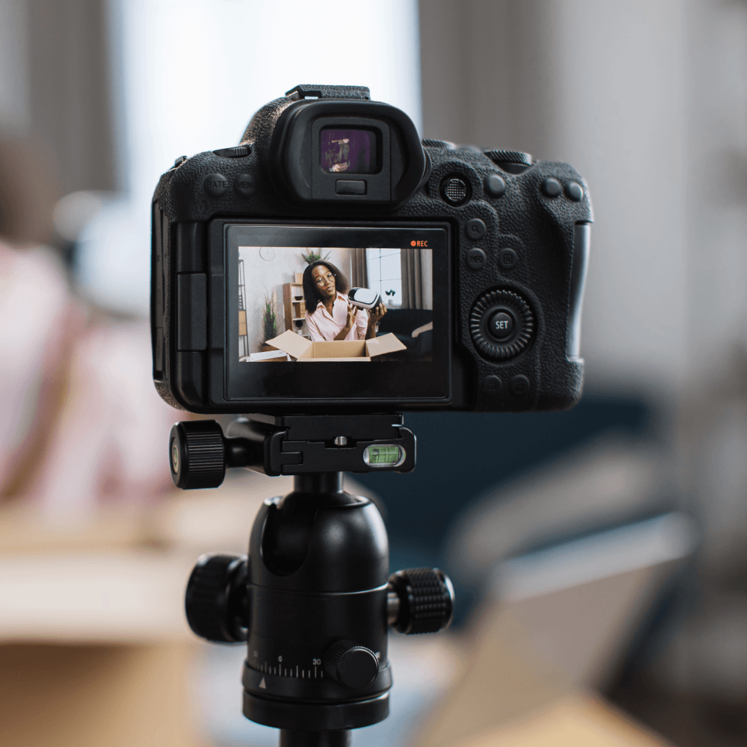 A camera on a tripod, its screen showing a woman being filmed indoors.