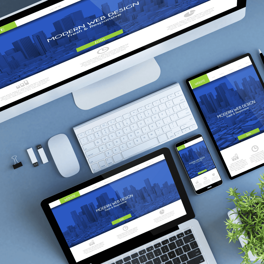 The same responsive website design shown on a desktop monitor, tablet, phone and laptop, laid out on a blue desk.