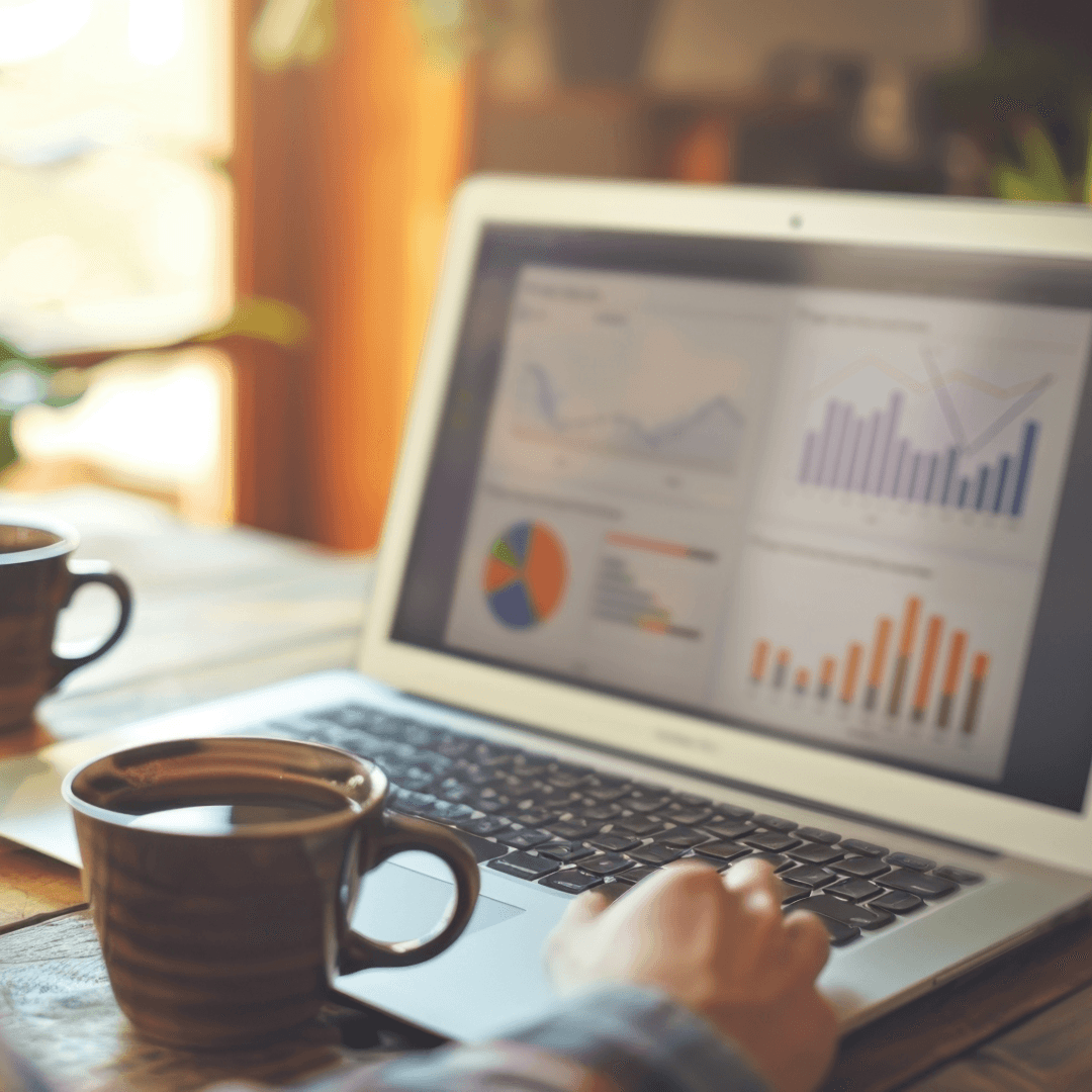 A laptop showing marketing analytics charts on a table, with two mugs of coffee beside it.