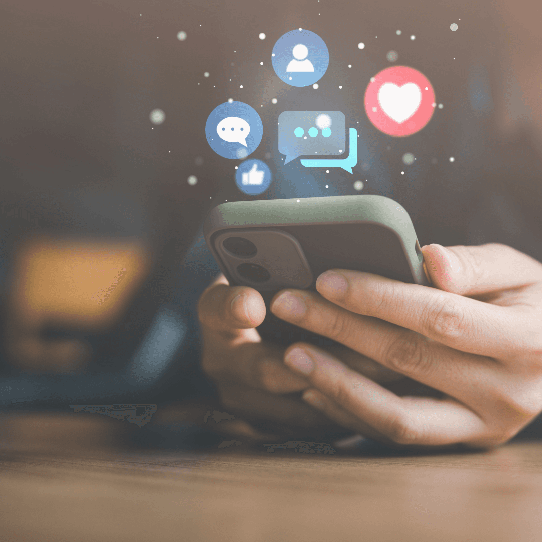 Hands holding a phone with social media reaction icons, likes, hearts and comments, floating above the screen.