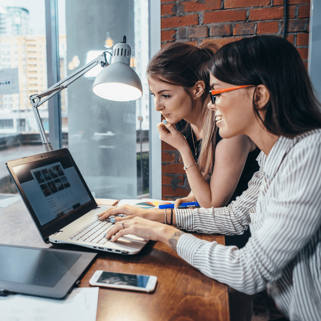 Two colleagues working together at a laptop by an office window.
