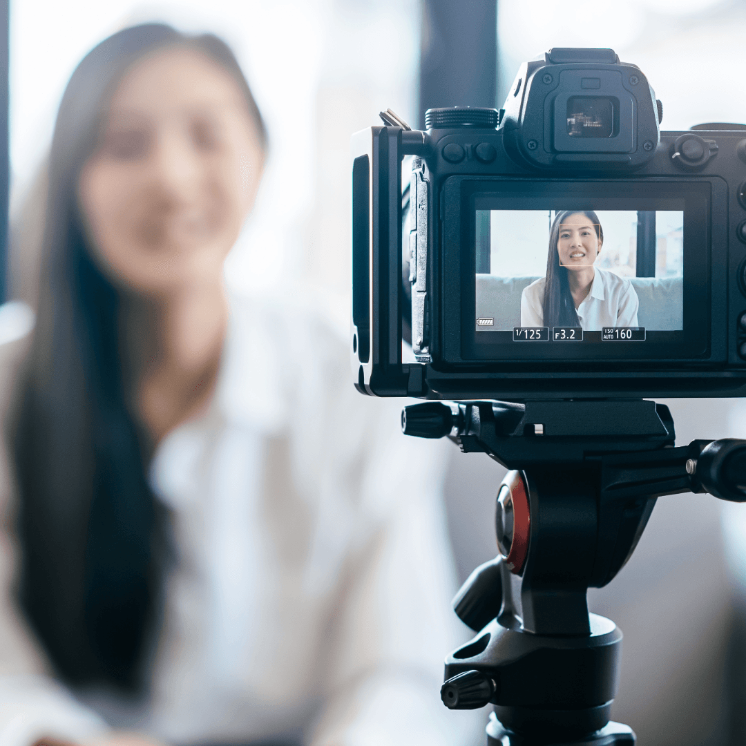 A camera on a tripod filming a woman speaking to camera, her image visible on the screen.