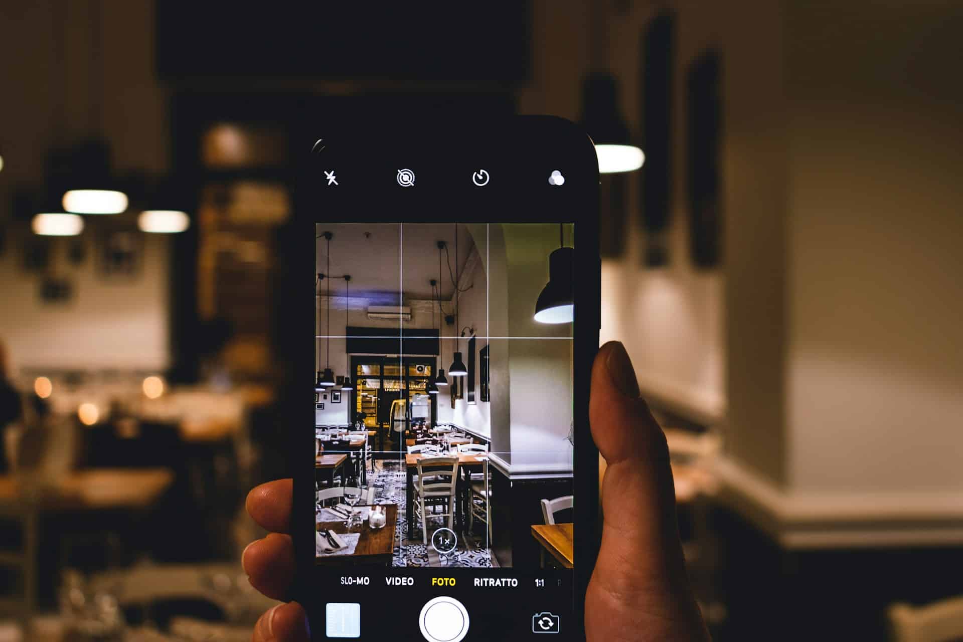 Close-up image of a hand holding a mobile phone up in a cafe taking a photograph. User-Generated Content for Small Businesses.