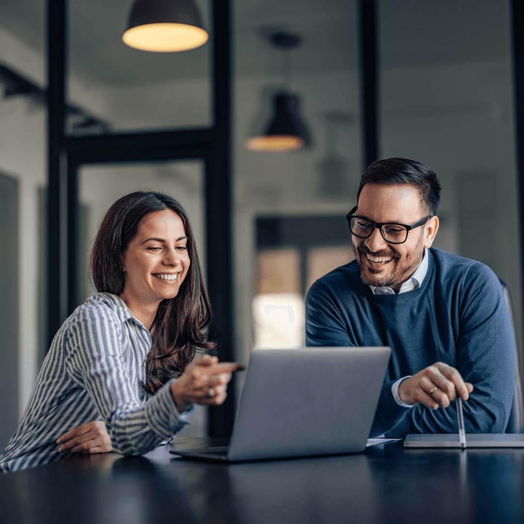 Two colleagues smiling as they look at a laptop together in a meeting room.