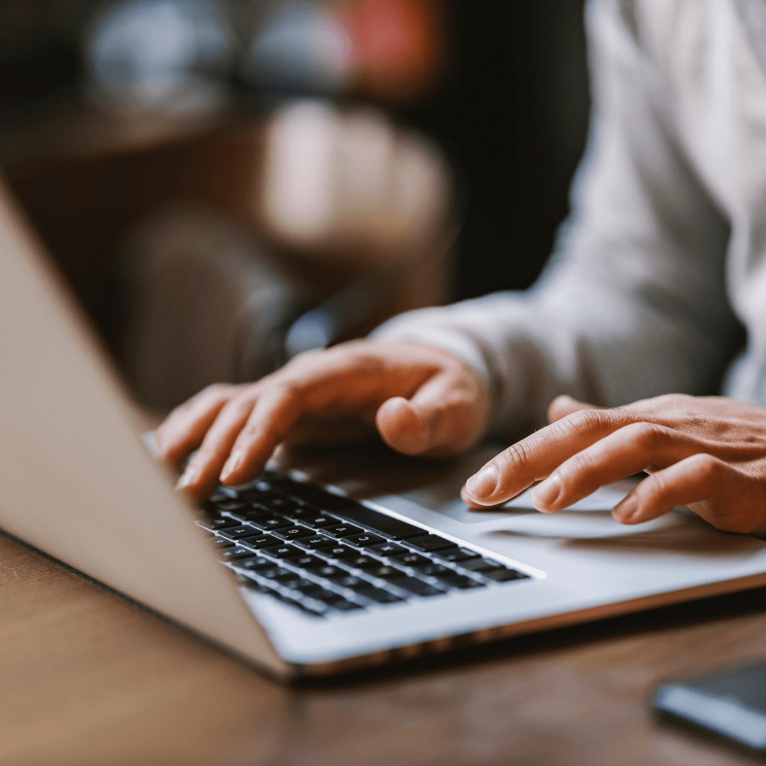 A person typing on a laptop at a wooden table in a cafe.