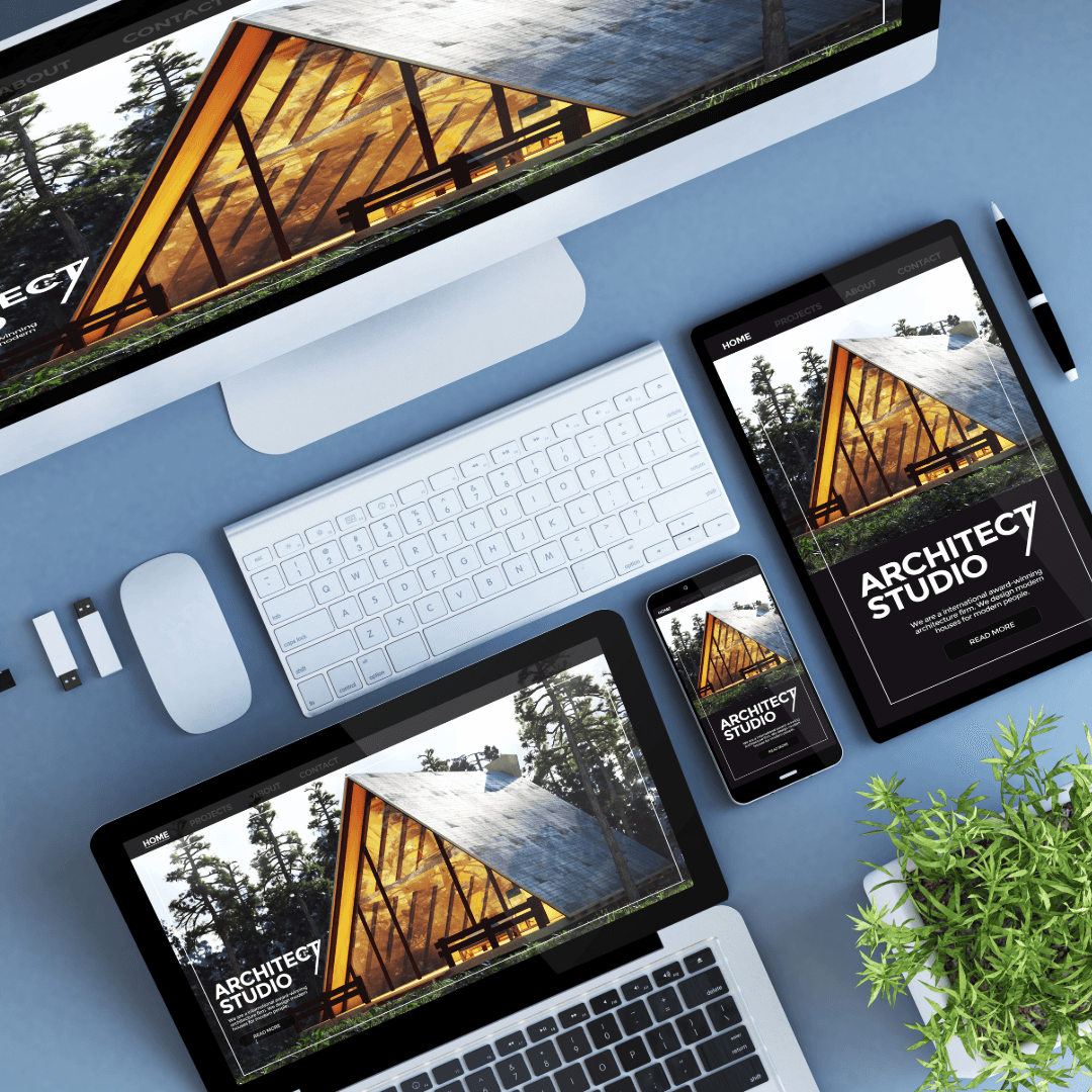 An architecture studio website shown on a desktop monitor, tablet, phone and laptop on a blue desk.