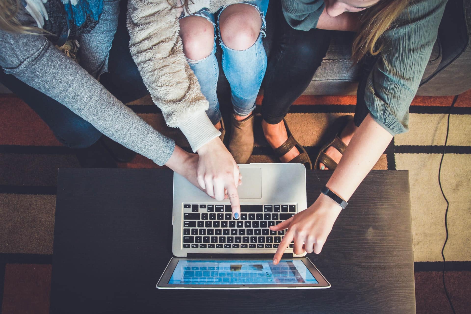 Overhead view of three people gathered around a laptop, one of them pointing at the screen.
