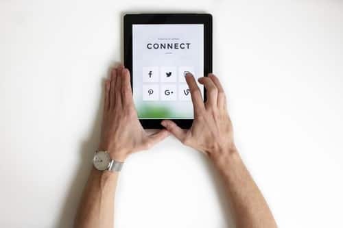 Overhead view of two hands holding a tablet showing a Connect screen with social media icons.