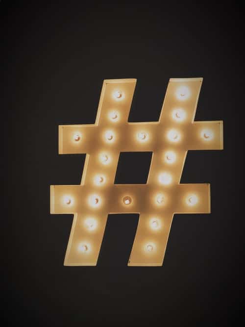 A large hashtag symbol made of illuminated fairground bulbs against a dark wall.