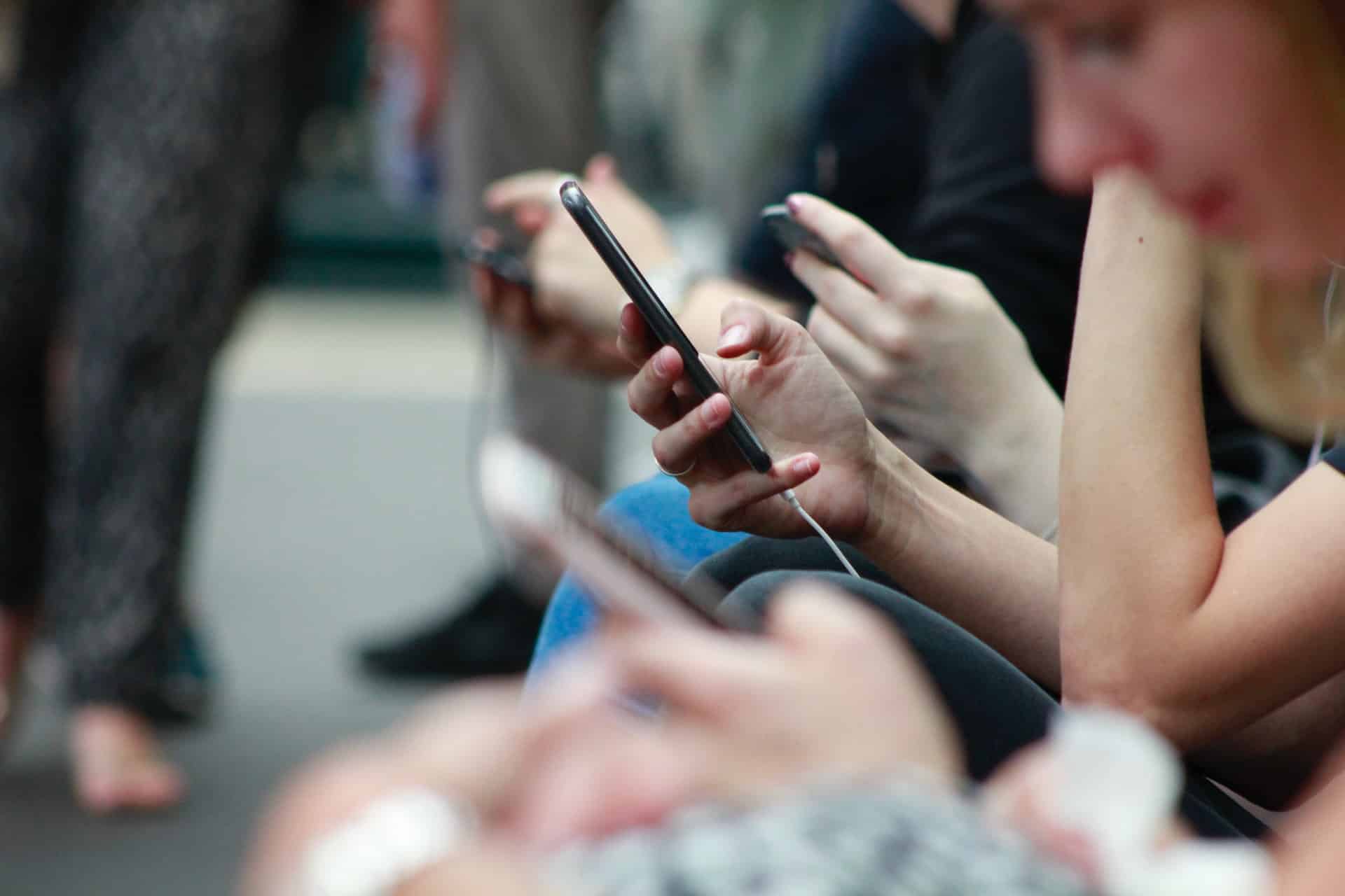 A row of people sitting side by side, each absorbed in their own smartphone.