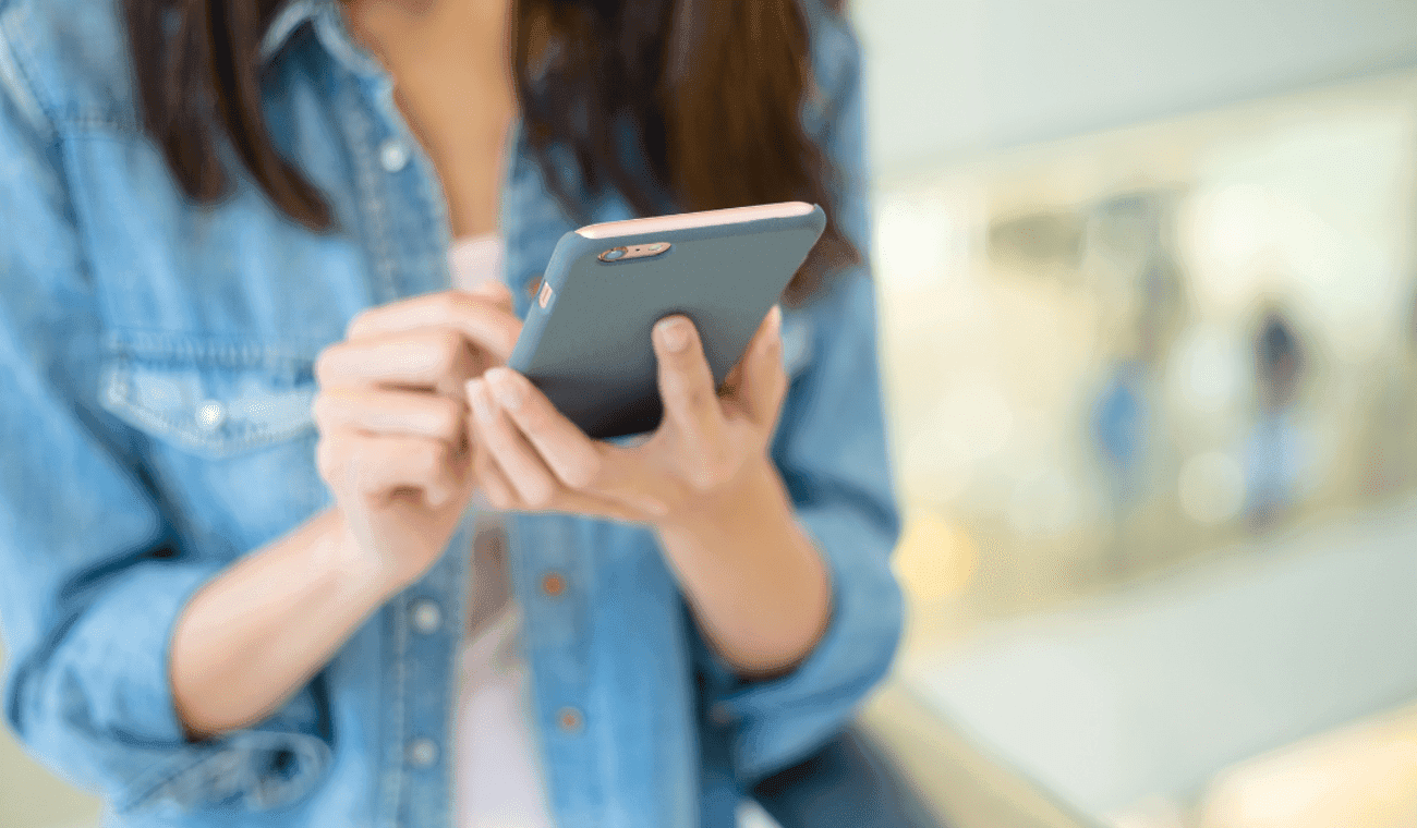 A woman in a denim jacket using a smartphone in a shopping centre.
