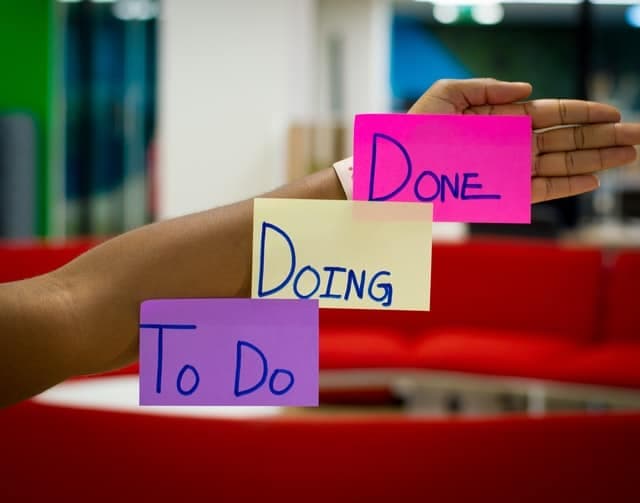 A hand holding three sticky notes labelled To Do, Doing and Done.