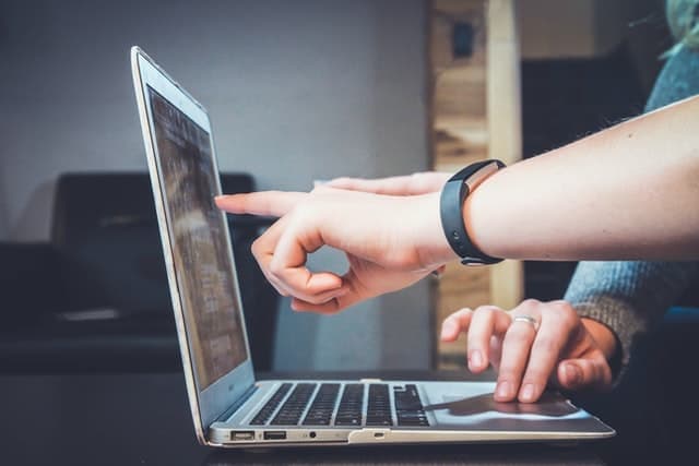 One person pointing at a laptop screen while another types, sitting side by side.