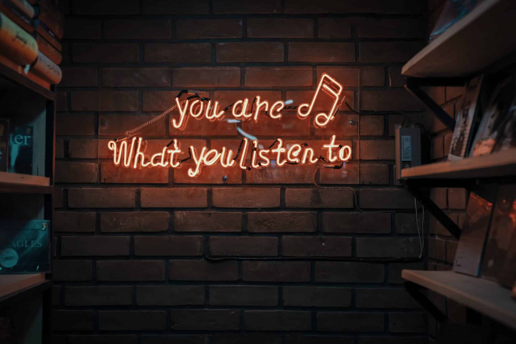 A neon sign on a brick wall reading You are what you listen to.