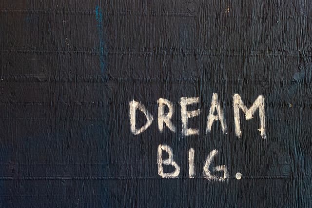 The words Dream Big written in chalk on a black painted wall.