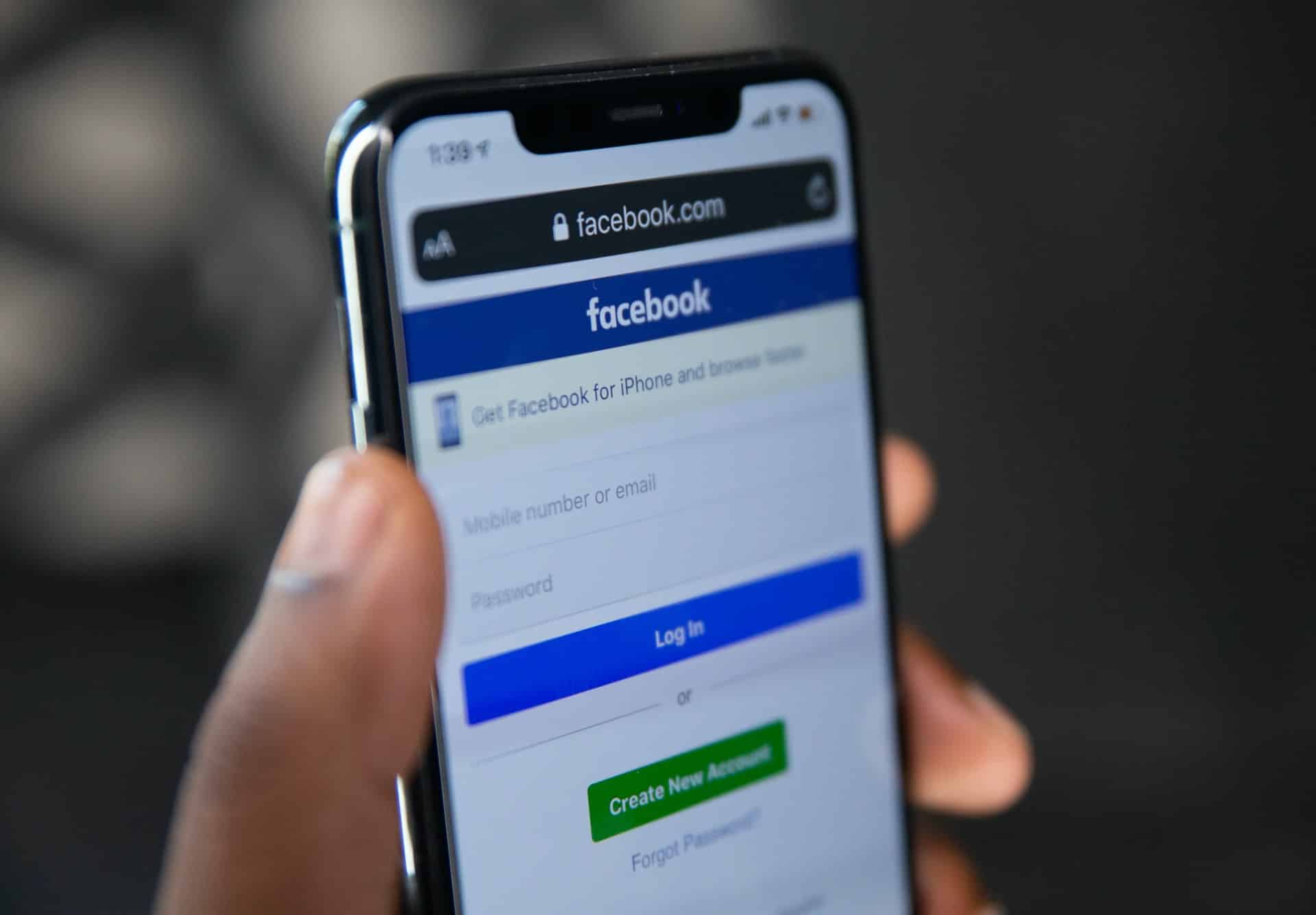 A hand holding a phone showing the Facebook login page.