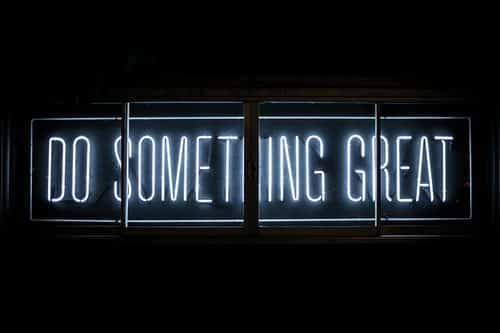 A white neon sign in a dark window reading Do Something Great.