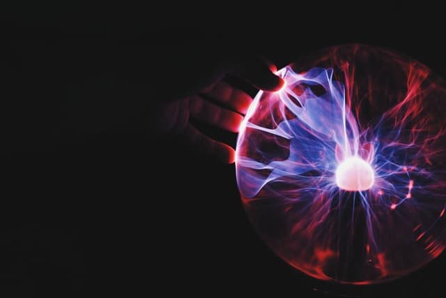 A hand resting on a plasma ball, with filaments of light reaching towards the fingers.