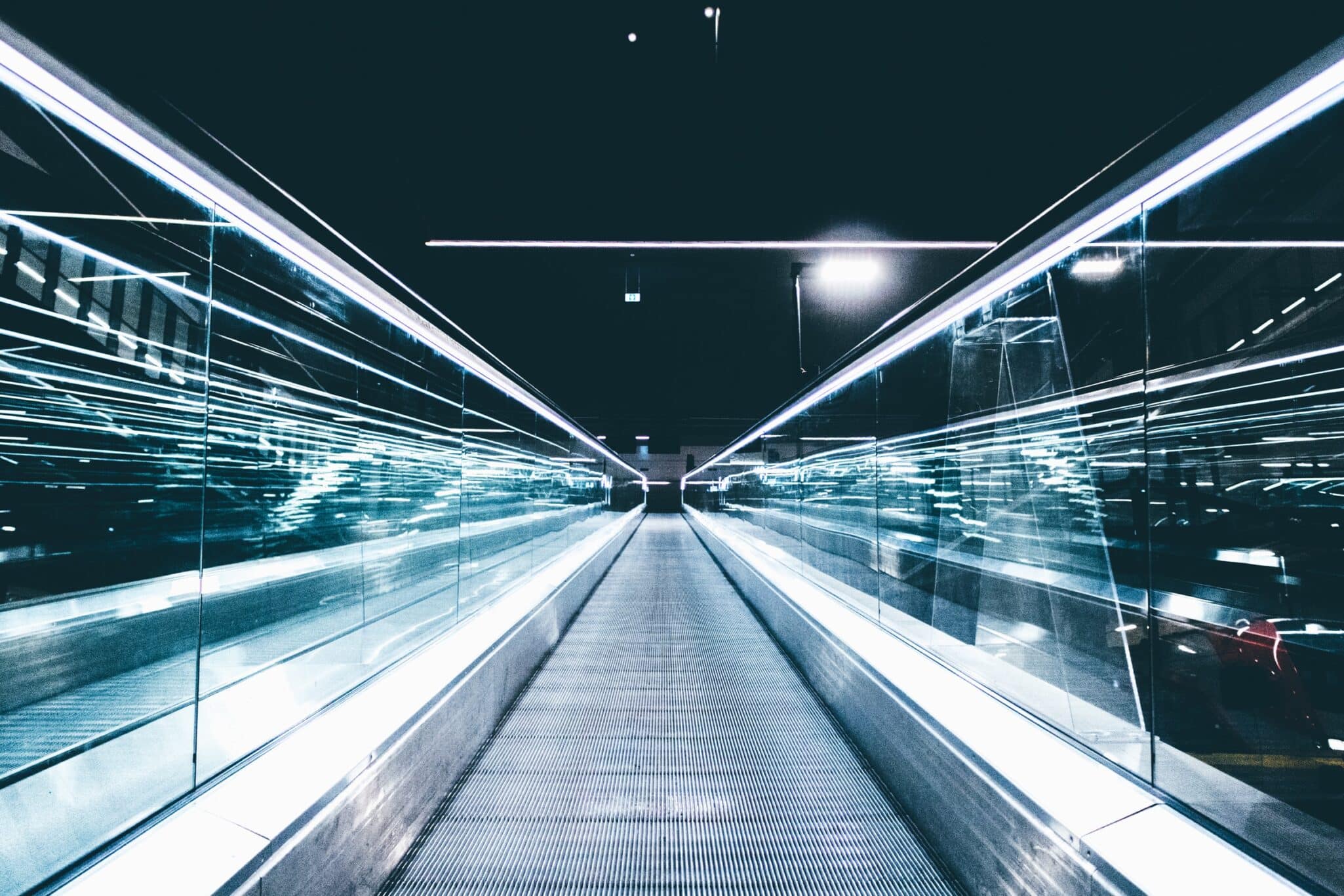 A moving walkway in an airport, lit by streaks of light in a long exposure.