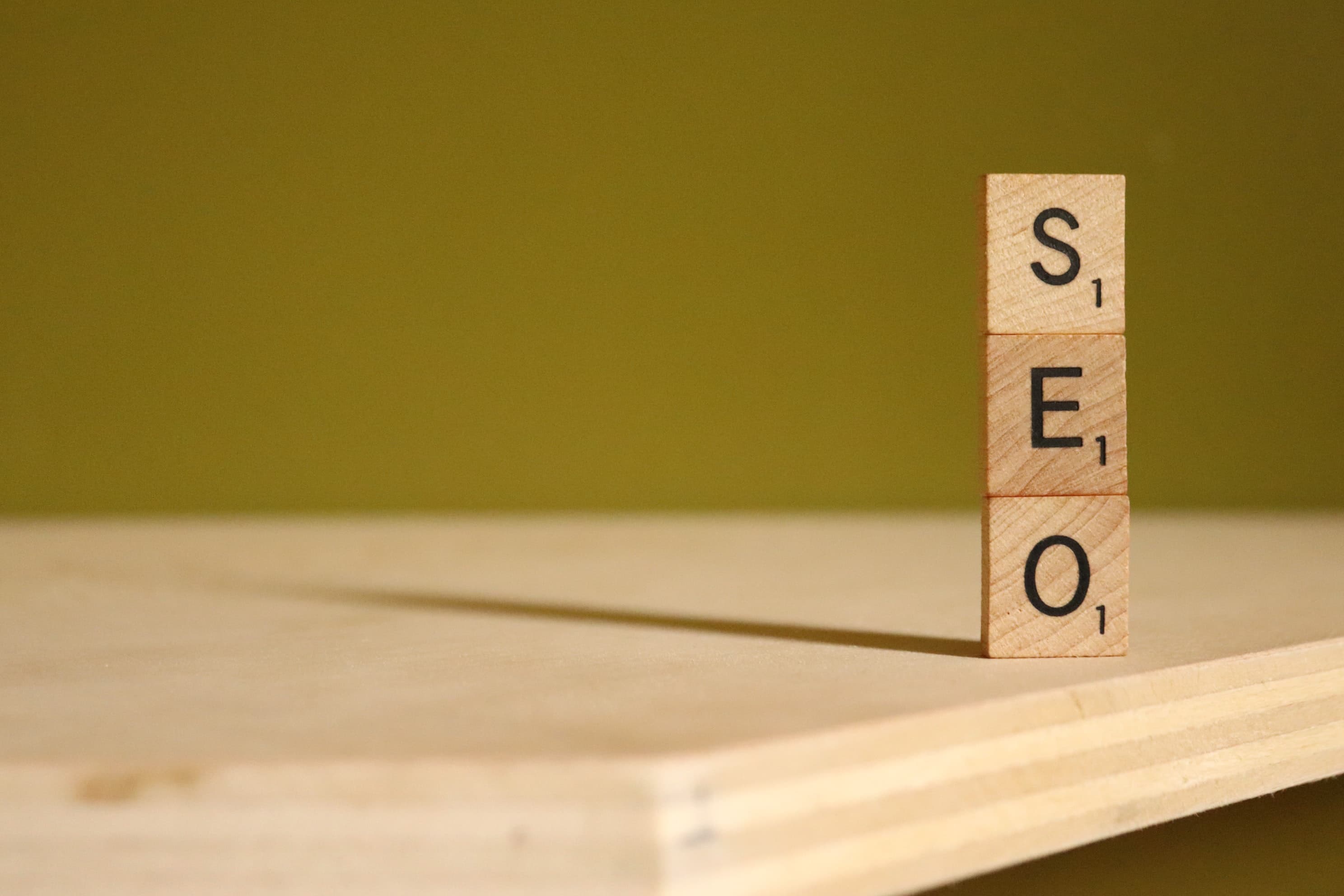 Three lettered tiles stacked on a plywood shelf spelling SEO.