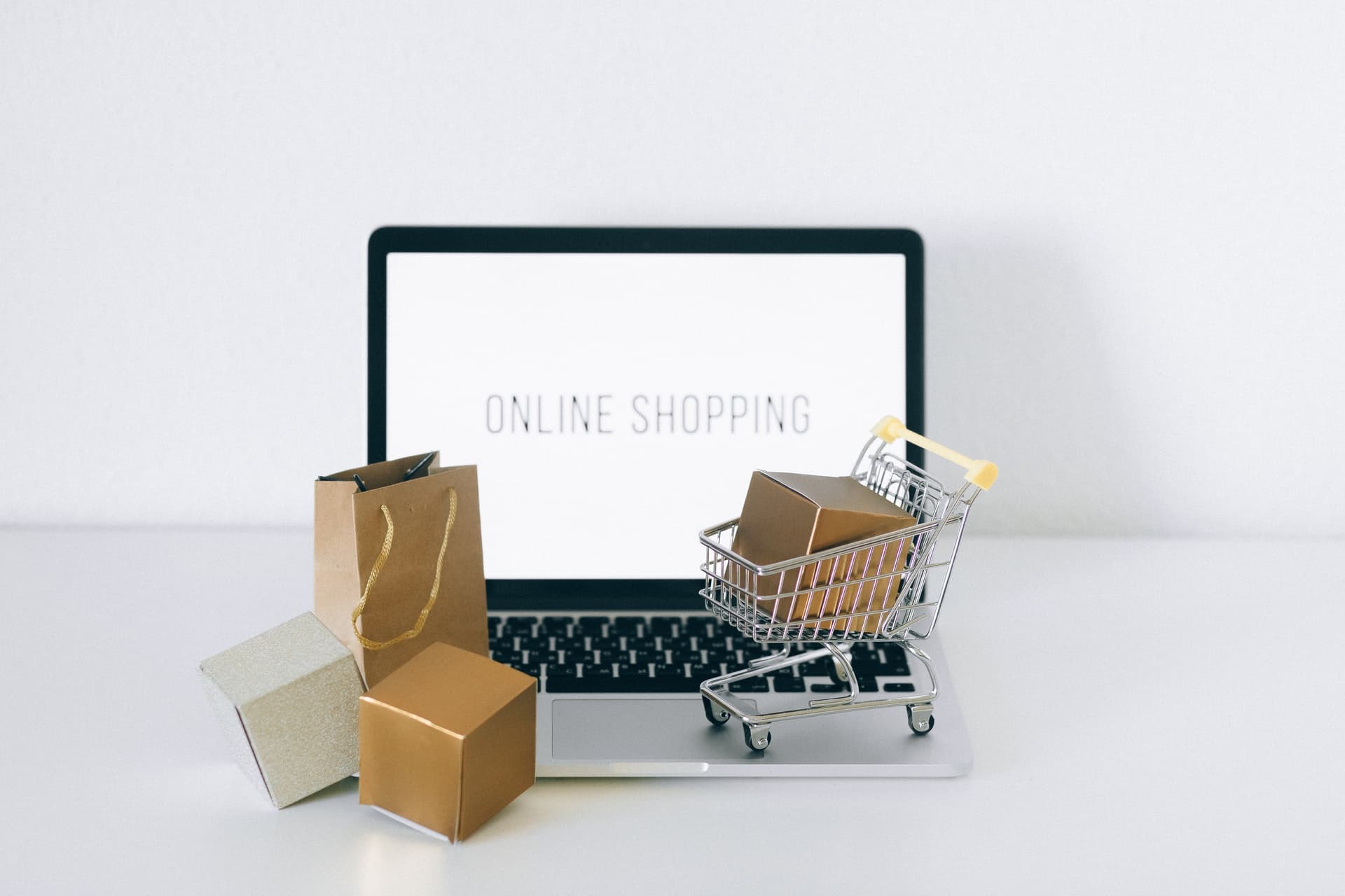 A laptop displaying the words Online Shopping, with a miniature trolley and parcels in front of it.