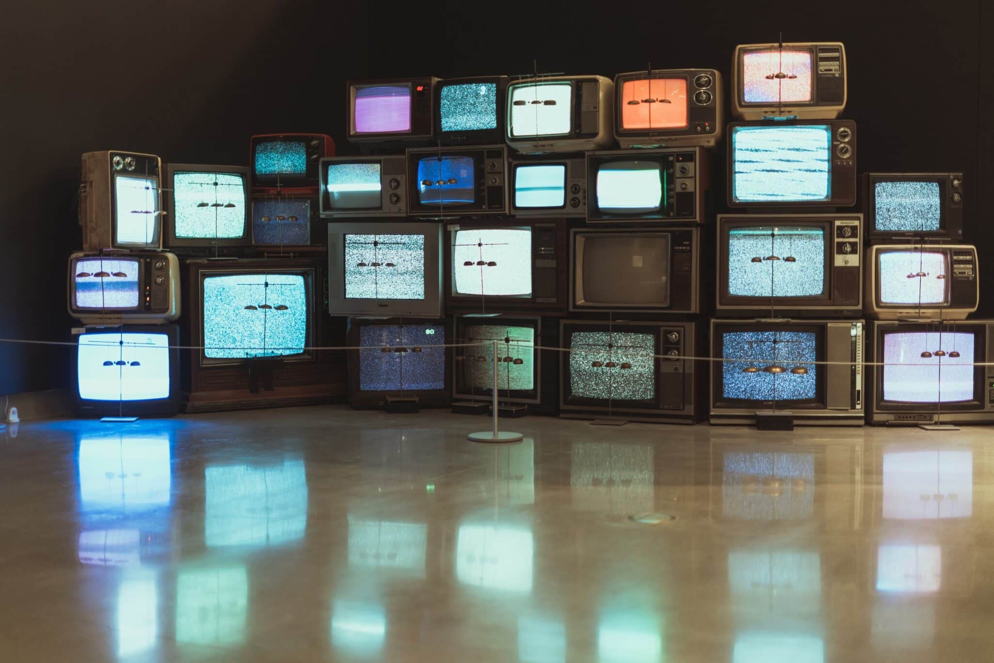 A stack of vintage televisions showing test cards in a dark room.